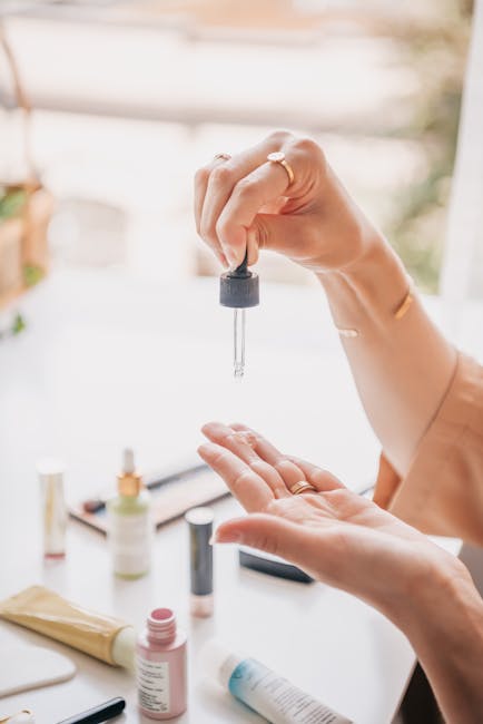 Close-up of hands using a dropper to apply serum as part of a skincare routine with various products nearby.